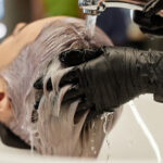 Closeup of unrecognizable hairstylist washing hair of young woman in salon sink and giving haircare treatment for bleached hair